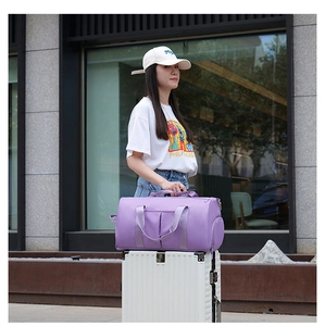 Purple fitness travel bag shown attached to a white luggage handle in outdoor setting