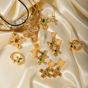 Detail of 18K gold-plated stainless steel cross necklaces and rings on beige silk fabric