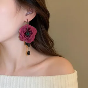 Elegant deep red fabric rose drop earrings with black waterdrop charms on a model