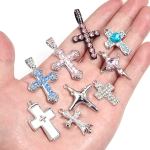 Assorted colorful rhinestone and pearl cross pendants held in hand for DIY necklaces
