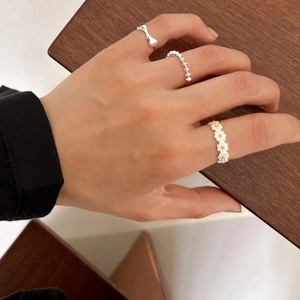 Detail showing stacked daisy and wave rings on finger with premium silver finish