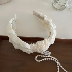 Detailed macro view of cream-colored pleated chiffon headband texture with elegant pearls