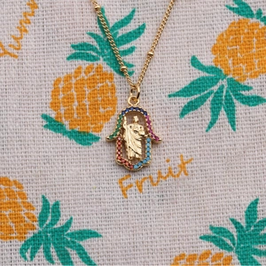 Golden Hamsa Hand necklace with colorful stones and relief charm on pineapple fabric