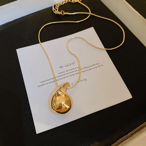 Macro detail of a polished gold teardrop pendant necklace on a minimalist jewelry card