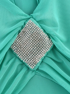 Detail eines türkisblauen Netz kleids mit Plisseestoff und funkelnder Diamantschnalle
