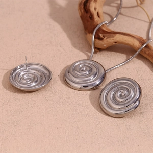 Detailed view of silver swirl texture necklace and spiral earrings on sand stone background