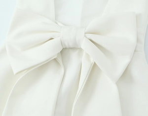 Detail shot of the textured white woven fabric and the oversized bow design on the dress