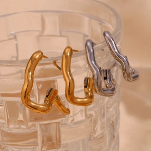 Macro view of gold and silver irregular wave hoop earrings on a glass rim