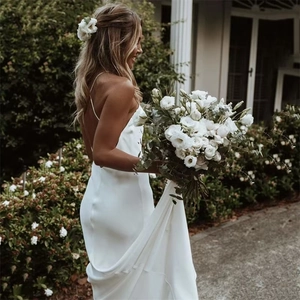 Elegant white satin deep V-neck bridal gown with open back and flowing skirt outdoors