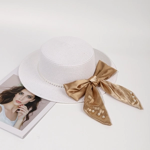 Close-up of white woven straw hat featuring a gold satin bow and pearl details