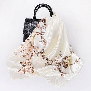 Elegant cream silk square scarf with vintage floral pattern draped on a black handbag
