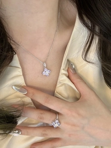 Close-up of a silver four-leaf clover necklace and ring set with sparkling purple zircon