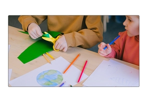 Children using safety scissors and colored pencils for creative paper craft on wood table