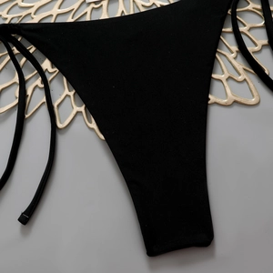 Detailed macro view of black bikini bottoms with adjustable side tie strings on golden plate
