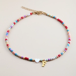 Detail of colorful beaded necklace with white heart bead and gold letter F pendant