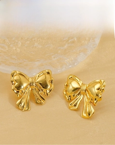 Detail of gold bow earrings with heart texture on silk fabric background