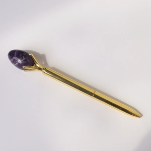 Macro detail of a golden metal ballpoint pen with a purple crystal gemstone top decoration