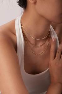 Detailed view of layered gold chain necklaces with pearls on a model's neck