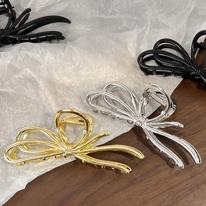Three elegant metal bow hair claws in gold, silver, and black on a textured surface