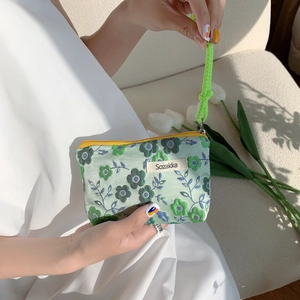Detail of floral makeup bag with green strap and zipper closure held by hand