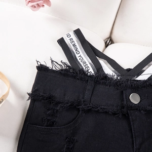 Dettaglio di pantaloncini in denim nero con bordi sfrangiati ed elastico stampato
