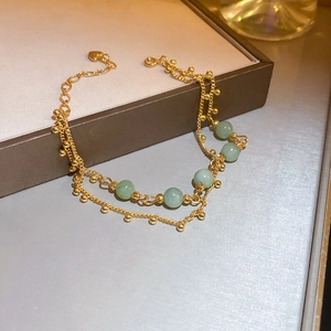 Detail of double-layer gold chain bracelet with green beads and heart pendant