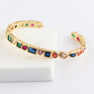 Golden open bangle with colorful rainbow zircons in various geometric shapes on white background