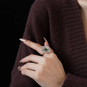 Close-up of a silver ring featuring a green square gemstone in a floral setting on model