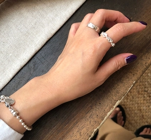 Detailed view of sterling silver heart tag bracelet and textured band rings on hand