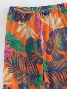 Detail view of vibrant orange tropical leaf print mesh pants with breathable texture