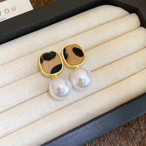 Close-up of leopard print square stud earrings with hanging pearl on velvet tray