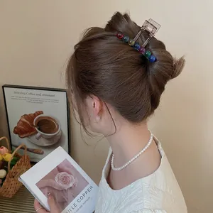 Acrylic hair claw clip with colorful round beads shown on a hair bun in a cozy setting