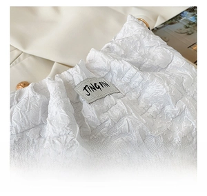 Detailed macro view of white pleated fabric texture and luxury label on the small square bag