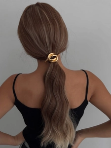 Detailed view of an elegant golden alloy bow-knot hair tie on a brown ponytail