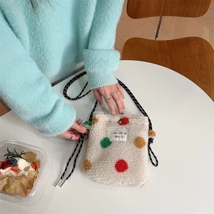 Détail du sac bandoulière en peluche à pois colorés posé sur une table blanche pure