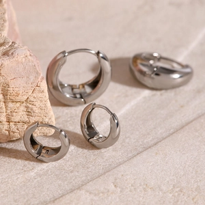 Minimalist silver stainless steel hoop earrings with polished dome design on stone background