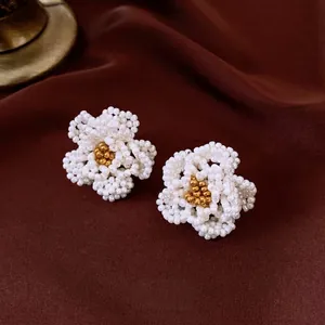 Elegant white camellia beaded earrings set with gold accents on red silk background