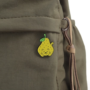 Detail of cute yellow pear-shaped cat enamel pin on a green canvas fabric bag