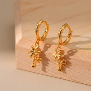 Close-up of golden palm tree charms on gold hoop earrings over a light wooden stand