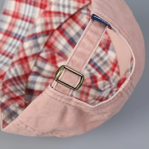 Detail of pink cotton baseball cap featuring checkered brim lining and metal buckle strap