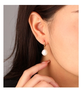 Macro shot of natural baroque pearl earrings with gold hooks on a model's ear