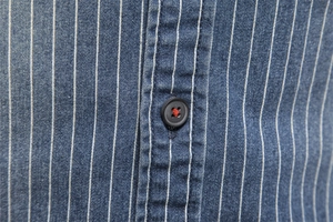 Macro view of blue striped denim shirt featuring black buttons and red cross-stitch detail