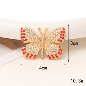 Detailed view of 4cm gold butterfly charm with red and white rhinestones on beige background