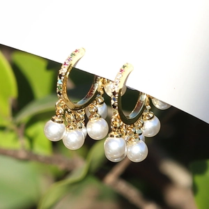 Detail of gold hoop earrings with multi-colored gems and elegant white pearl tassels