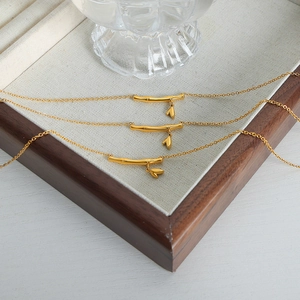 Trois colliers dorés en forme de bambou avec pendentifs cœur sur un plateau en bois