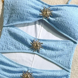 Detail of light blue textured swimwear featuring cut-outs and golden sun metal accents