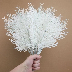 Artificial white cypress branch for Christmas DIY decor held against a brown background