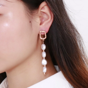Gros plan de boucles d'oreilles élégantes en perles baroques et maillons carrés dorés