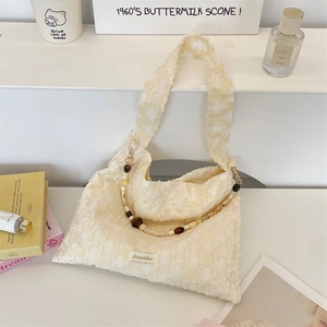Detailed view of cream jacquard shoulder bag featuring texture and beaded chain