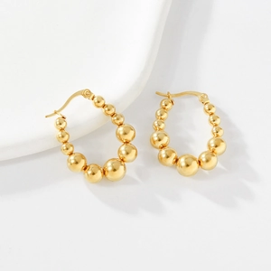 Macro shot of gold beaded hoop earrings with gradient size beads on ceramic